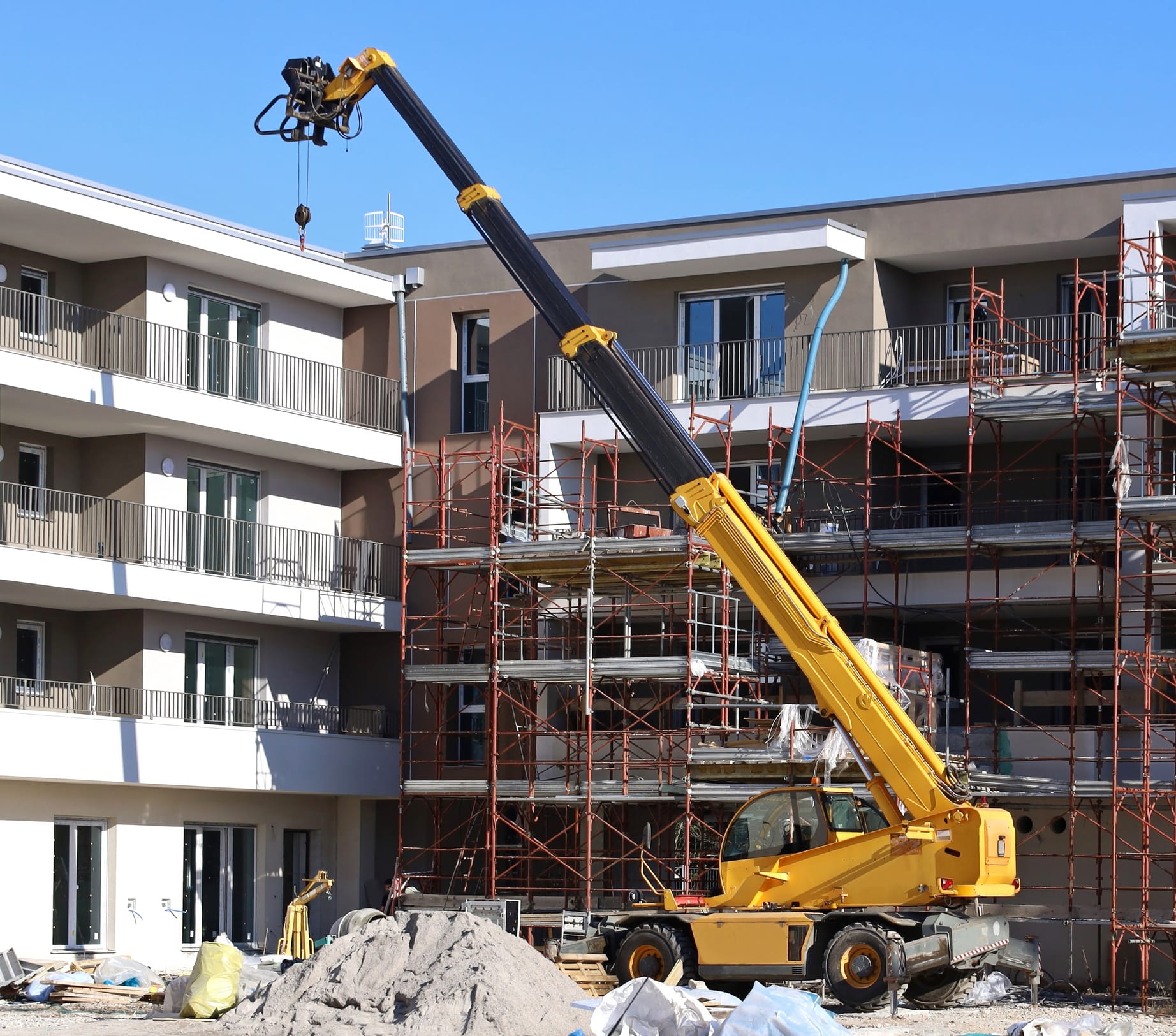 Gelber Teleskoplader bei der Arbeit vor zwei neuen Gebäuden im Bau.
